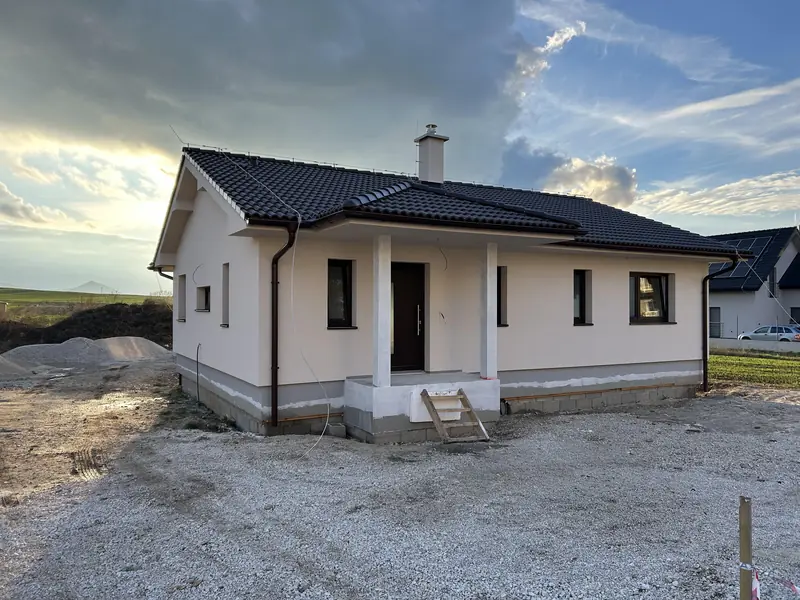 Biely bungalov s tmavou valbovou strechou a krytým vstupom